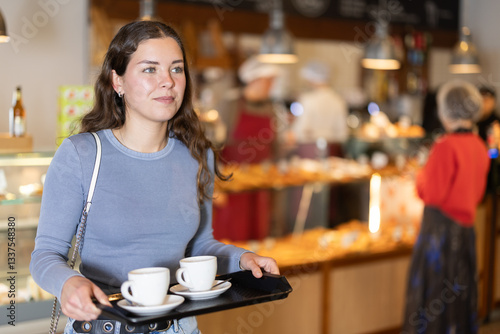 Positive girl carries tray with two cups of coffee in cafe interior
