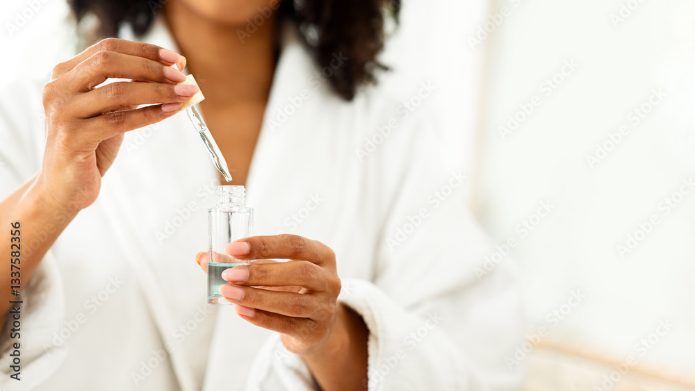 Fototapeta premium Essential Oils Benefits. Bottle With Organic Serum In Hands Of Unrecognizable Black Woman Making Beauty Treatment After Shower, Cropped Image, Closeup