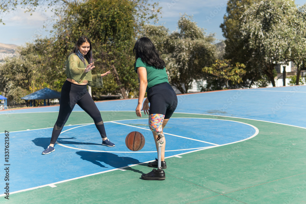 Obraz premium Young women playing basketball, one with prosthetic leg dribbling ball on outdoor court