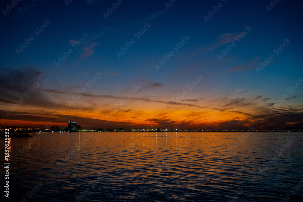Obraz premium Tranquil Twilight Over the Arabian Gulf with a Crescent Moon and Vibrant Sunset Reflections in Kuwait