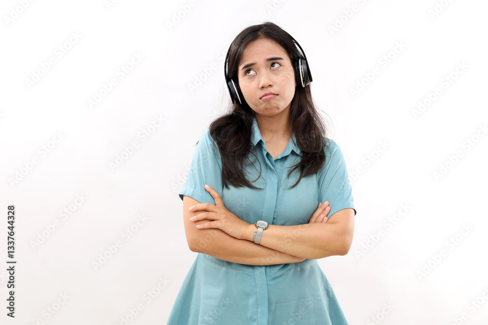 Frustrated disappointed Asian woman has gloomy sad expression keeps arms folded concentrated thoughtfully away listens music via wireless headphones wears casual shirt isolated on white studio wall Frustrated disappointed Asian woman has gloomy sad expression keeps arms folded concentrated thoughtfully away listens music via wireless headphones wears casual shirt isolated on white studio wall
