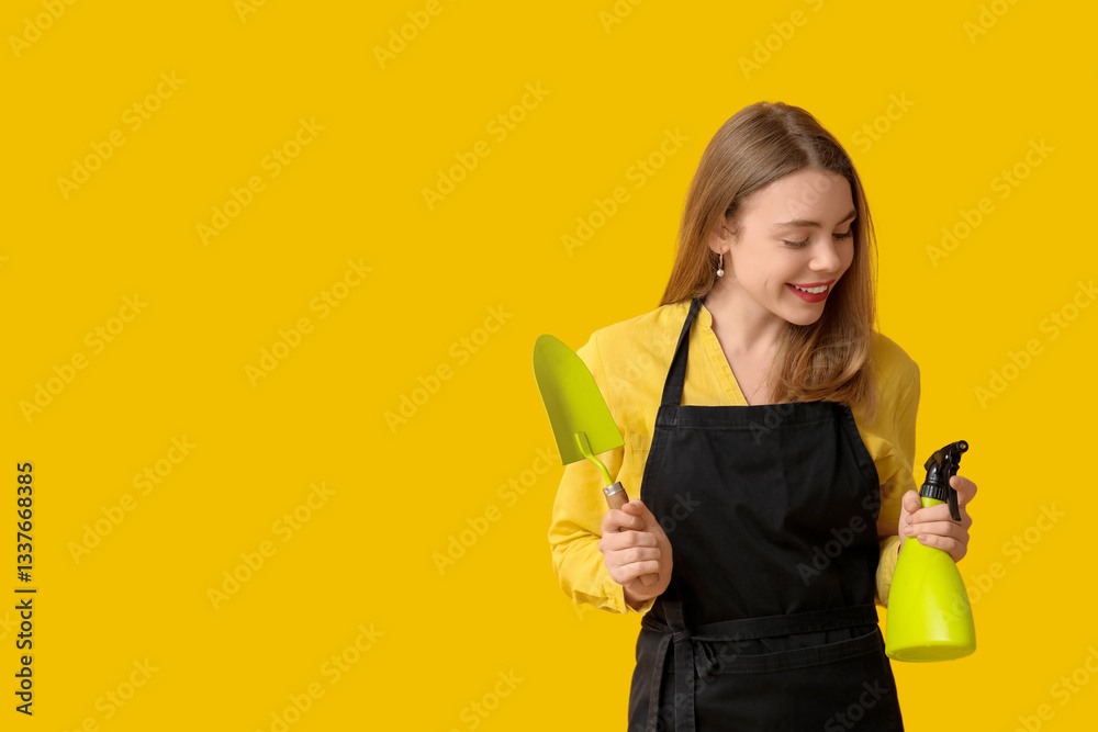 Beautiful young woman with water sprayer and gardening shovel on yellow background Beautiful young woman with water sprayer and gardening shovel on yellow background