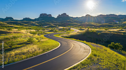 An asphalt road winding through the landscape, with mountains in the background and green grass on both sides