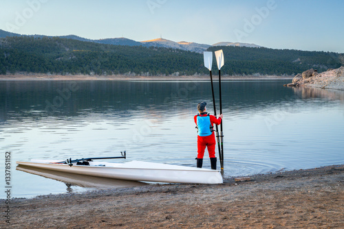 male rower and a coastal rowing shell on a rocky shore of Carter Lake in fall or winter scenery in northern Colorado.