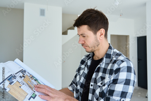 Obraz na płótnie Thoughtful man examines a floor plan while standing in unfinished home. Male home owner analyzing architectural blueprint in new apartment. Interior design and renovation decisions concept w salonie