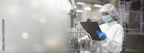 A woman in a white lab coat and blue gloves is looking at a clipboard. She is wearing a face mask.