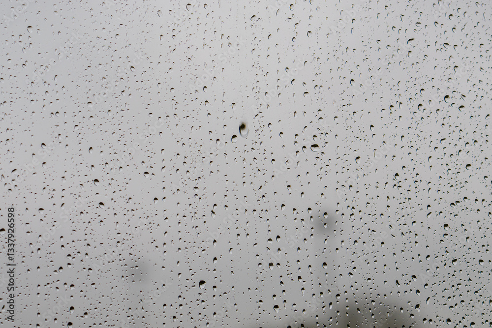 Raindrops on window glass against the moody grey British sky create a natural pattern. Water droplets on a transparent surface capture the minimalist texture during typical overcast weather Raindrops on window glass against the moody grey British sky create a natural pattern. Water droplets on a transparent surface capture the minimalist texture during typical overcast weather