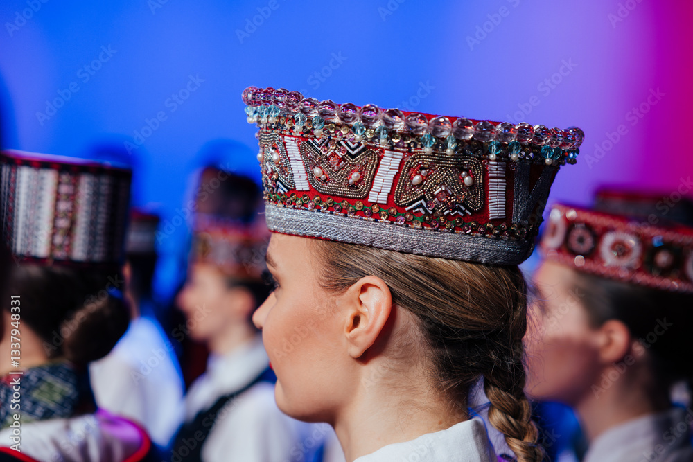 Fototapeta premium A close-up of a woman wearing an ornate beaded traditional Baltic headdress during a cultural performance, surrounded by others in similar folk attire