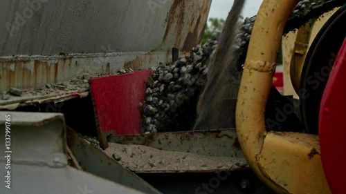 Crushed stone and sand being discharged from an industrial conveyor system at a construction site. Close-up view of heavy machinery in operation.