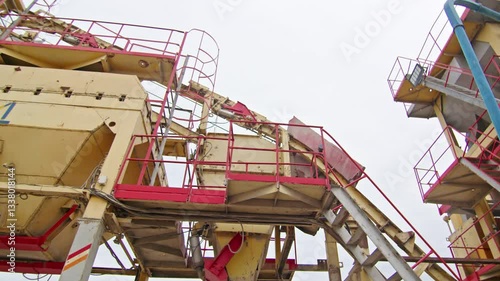 Industrial aggregate processing plant with conveyor system, metal platforms, and machinery. Large-scale construction and mining equipment for material handling