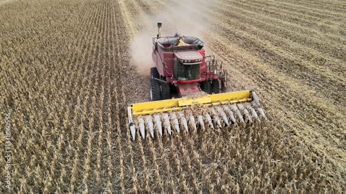 Large combine harvester works to clear crops in an agricultural field, dust and smoke rising behind as grain fills holding tank, aerial tracking