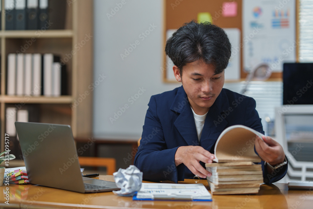 Office worker in a professional setting organizing a stack of documents. A laptop and crumpled paper are on the desk, suggesting a busy work environment with attention to detail Office worker in a professional setting organizing a stack of documents. A laptop and crumpled paper are on the desk, suggesting a busy work environment with attention to detail