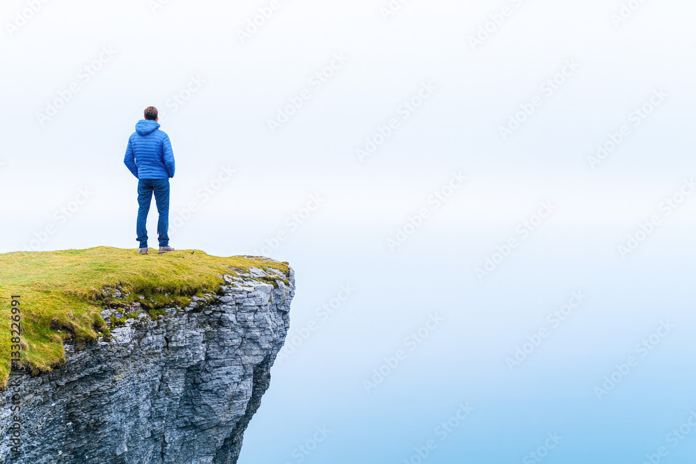 Obraz premium Solitary person standing on a cliff edge, gazing into the misty horizon, symbolizing contemplation, freedom, and vast possibilities. 