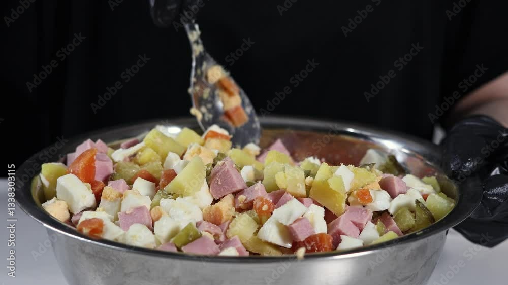 preparing olivier salad with diced potatoes, carrots, eggs, ham, and pickles in a large metal bowl before adding mayonnaise for a festive dish