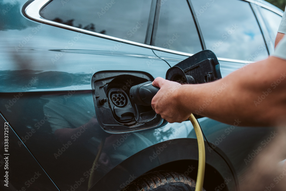 Obraz premium Man charging electric car, plugging charger in charging port.