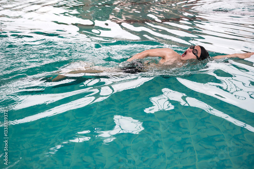 Male Asian swimmer with swim cap and goggles swimming freestyle in pool