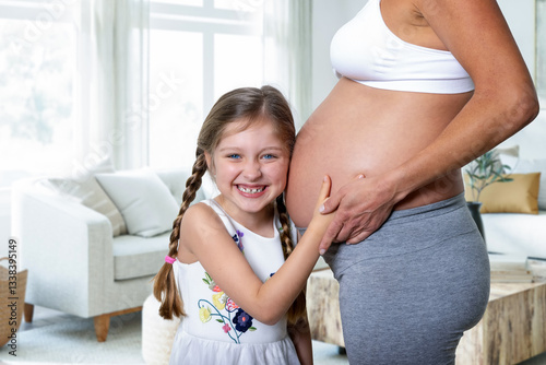 Obraz na płótnie A cute, happy daughter listening to the belly of her pregnant mother in anticipation of her brother or sister w salonie