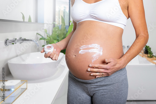 Obraz na płótnie Close-up view of a pregnant woman putting cream of her stretched belly skin in the bathroom w salonie