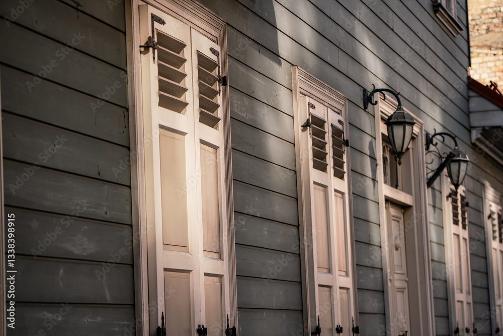 Fototapeta premium Vintage style wooden window shutters in white color on green wooden building in Riga, Latvia. Retro style Riga building. Sun shining sun rays on old wooden building