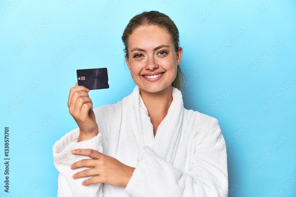 Blonde in bathrobe with credit card in blue studio happy, smiling and cheerful. Blonde in bathrobe with credit card in blue studio happy, smiling and cheerful.