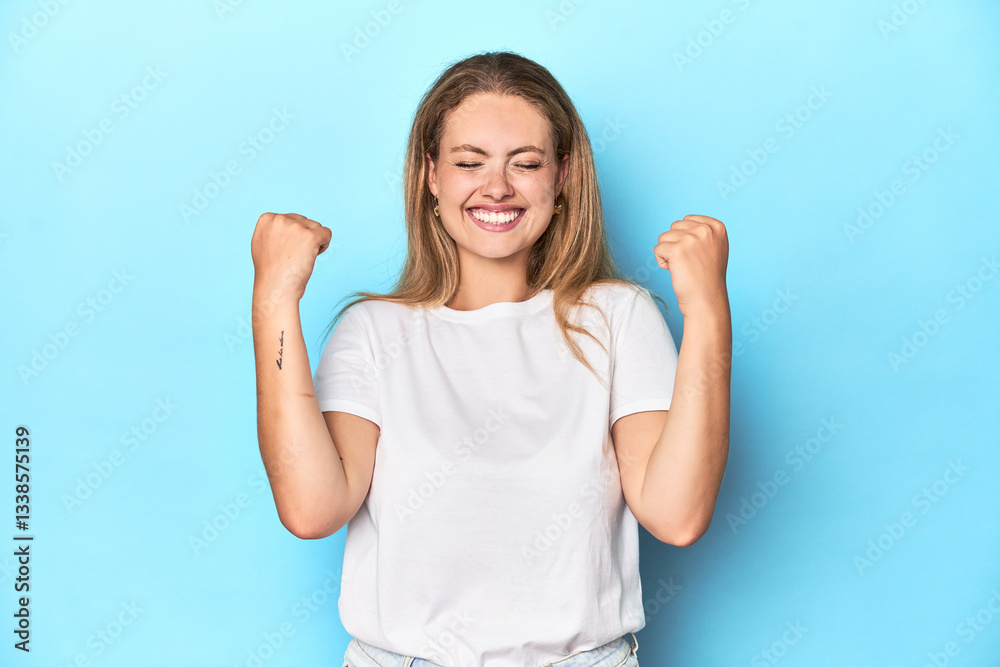 Fototapeta premium Blonde young woman in white t-shirt on blue background cheering carefree and excited. Victory concept.