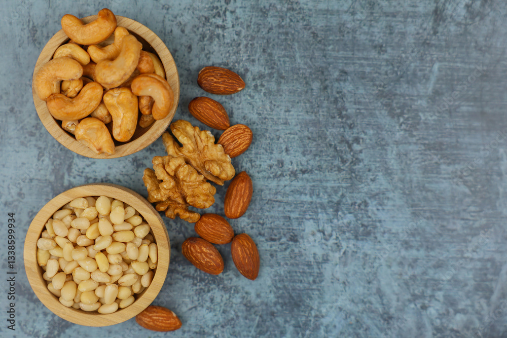 Close-up view from above of wooden bowls with pine nuts and cashews, which stand on the side surrounded by walnuts and almonds on a gray background with space for text. The concept of healthy snacks Close-up view from above of wooden bowls with pine nuts and cashews, which stand on the side surrounded by walnuts and almonds on a gray background with space for text. The concept of healthy snacks