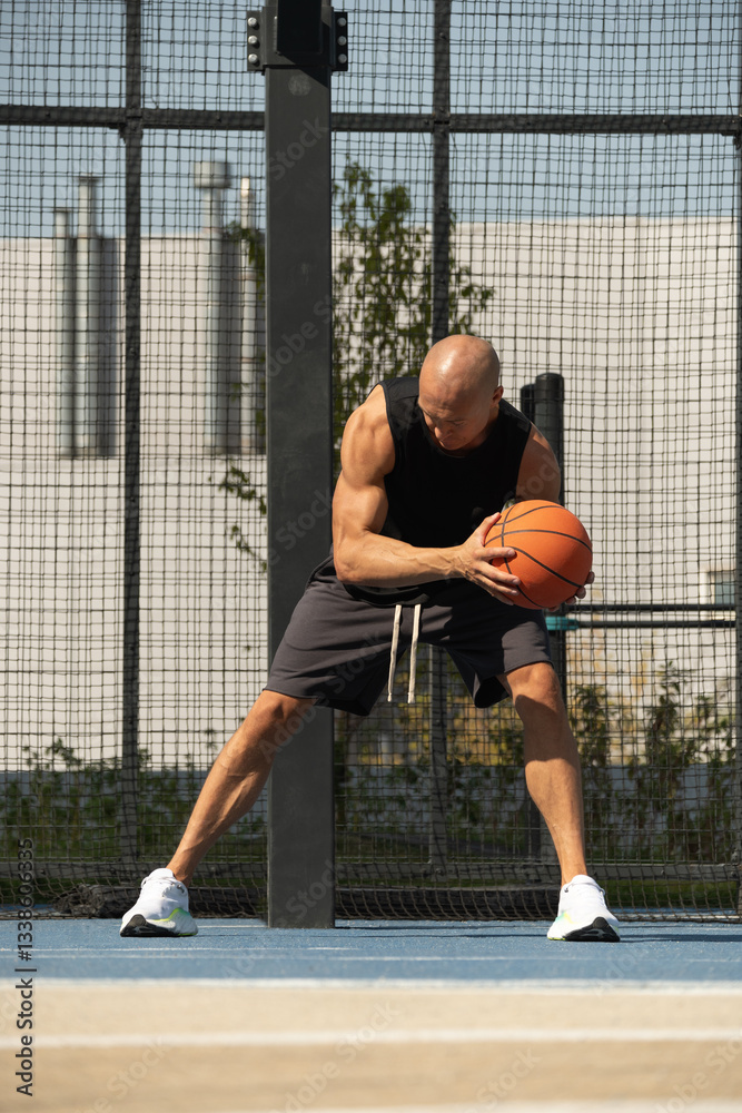 Sporty adult man playing with basketball ball on sports court at courtyard. Team sport. Basketball coach. Game moment.