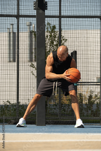 Sporty adult man playing with basketball ball on sports court at courtyard. Team sport. Basketball coach. Game moment.