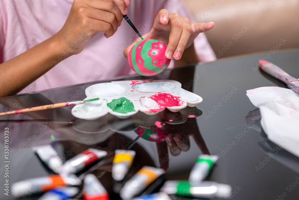 Obraz premium A little girl is painting on an egg with a paintbrush for easter egg decoration on the table. Concept of celebrating the easter holiday