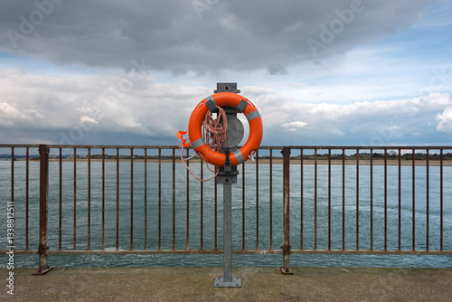 Orange lifebelt lifesaver on a railing by the sea