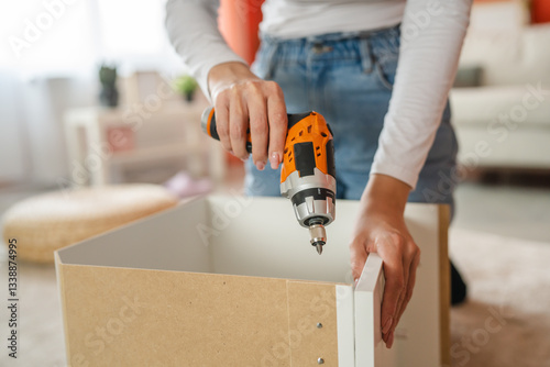 Woman assembling furniture with power drill at home