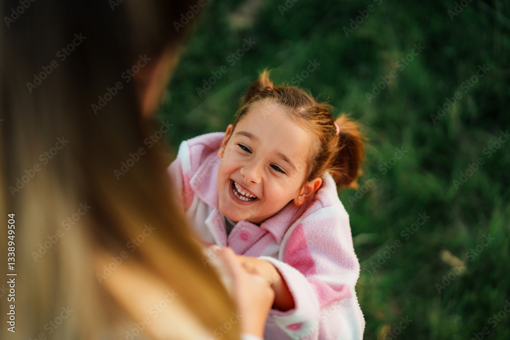 Cheerful little girl, wearing a pink pajama, is held by her mother, laughing heartily and enjoying a loving embrace in the beautiful outdoors, creating a heartwarming scene of family bonding Cheerful little girl, wearing a pink pajama, is held by her mother, laughing heartily and enjoying a loving embrace in the beautiful outdoors, creating a heartwarming scene of family bonding