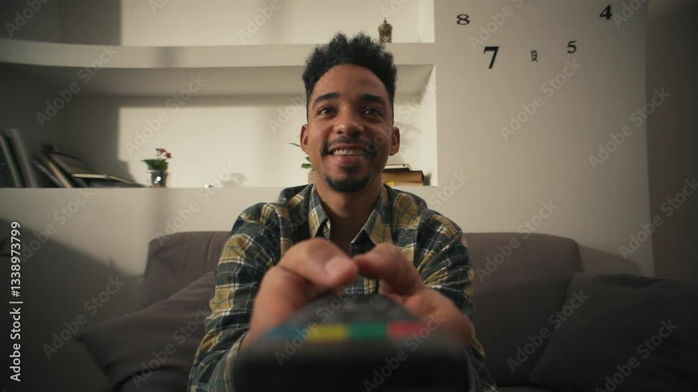 Smiling American man is sitting on couch with remote control and choosing movie.