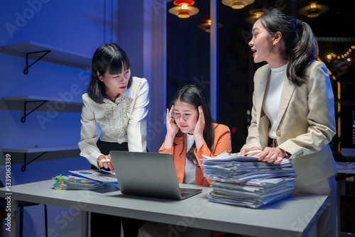 Asian businesswomen arguing and giving pressure to stressed colleague with a big stack of paperwork in office at night