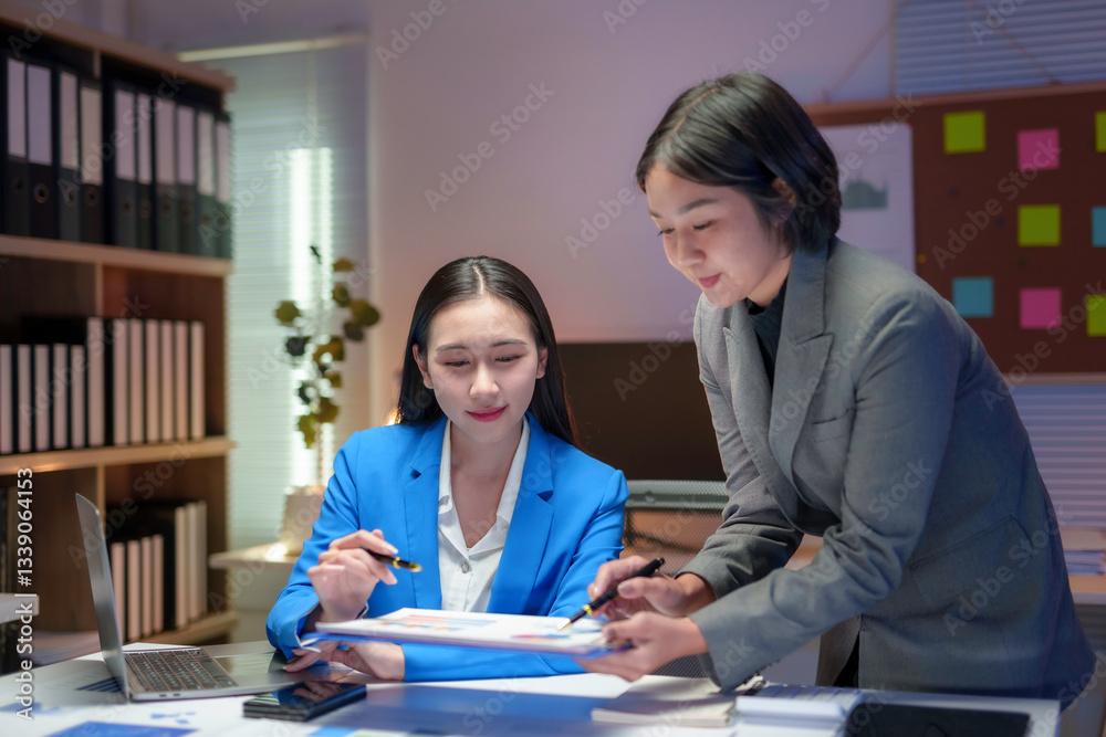 Obraz premium Two young Asian businesswomen are reviewing financial reports and working late in a modern office