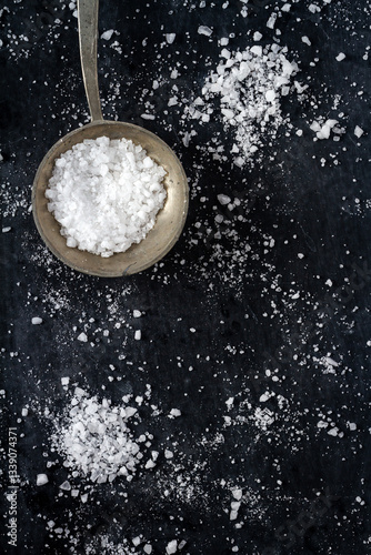 Top view of a spoon with coarse grained sea salt on black background. Flat lay. Top view. Food concept.