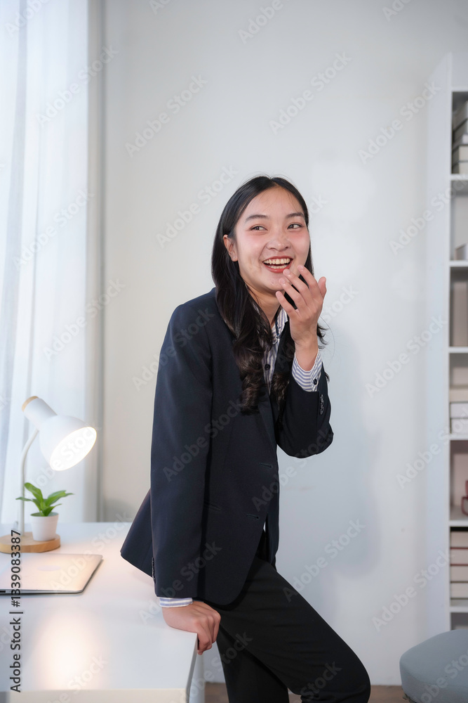 Professional Asian businesswoman smiling, leaning confidently near workspace with contemporary office background Professional Asian businesswoman smiling, leaning confidently near workspace with contemporary office background