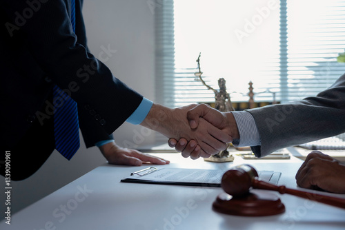Professional lawyers finalizing agreement, shaking hands near gavel and Lady Justice statue in law firm setting