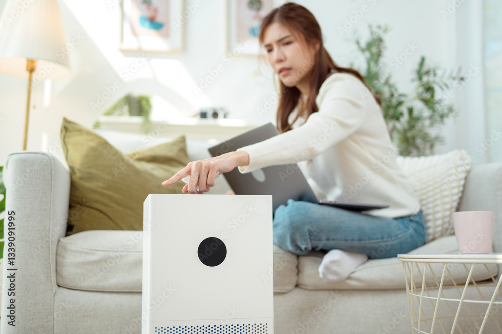 Woman Using Air Purifier While Working on Laptop in Cozy Living Room With Indoor Plants Woman Using Air Purifier While Working on Laptop in Cozy Living Room With Indoor Plants