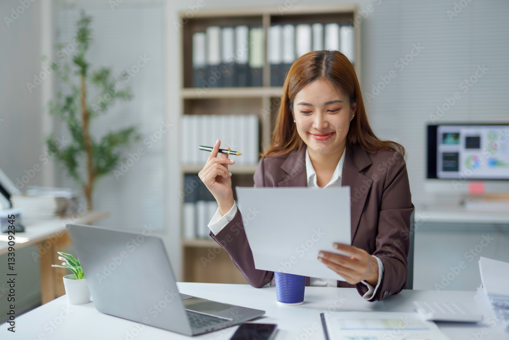 Professional businesswoman reviewing paperwork, writing notes, smiling warmly at workspace Professional businesswoman reviewing paperwork, writing notes, smiling warmly at workspace