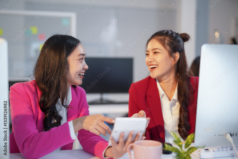 Two asian businesswomen laughing and working together using a calculator in a modern office Two asian businesswomen laughing and working together using a calculator in a modern office