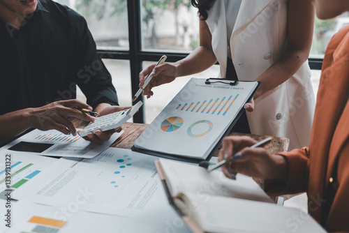 Business people working together analyzing financial charts and business graphs using calculator during a meeting in the office