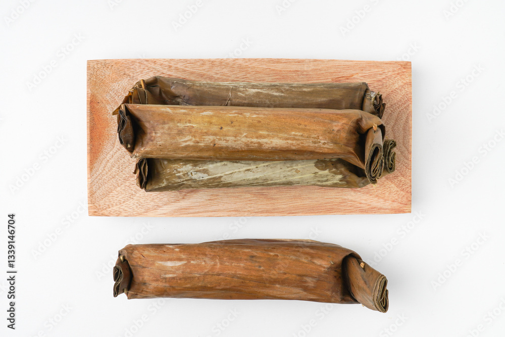 Fototapeta premium Lontong or rice cake on wooden plate. Traditional Javanese food made from steamed rice and wrapped in banana leaves. Isolated on white background, flat lay setup