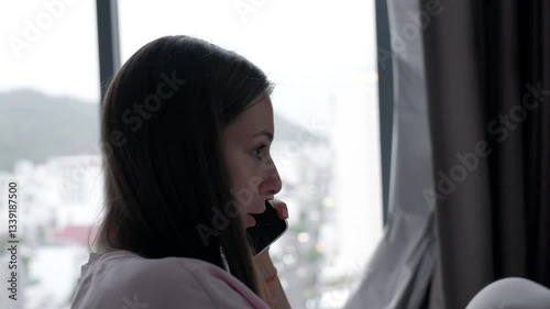 Close up portrait a woman speak on cell phone about work. Girl have call with client on background big city light. Business woman do business. Young woman talking on phone in hotel room at day.