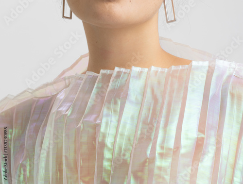 A woman in a shimmering, pleated top gently places her hand on her shoulder, capturing a moment of delicate grace.