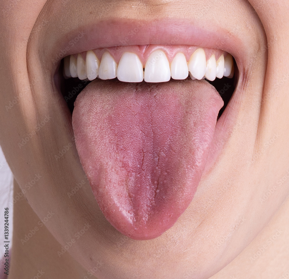 Obraz premium A close-up of a smiling mouth with a pink tongue sticking out, revealing white, well-aligned teeth. The tongue is slightly moist with visible texture, and the model's skin is fair and smooth.