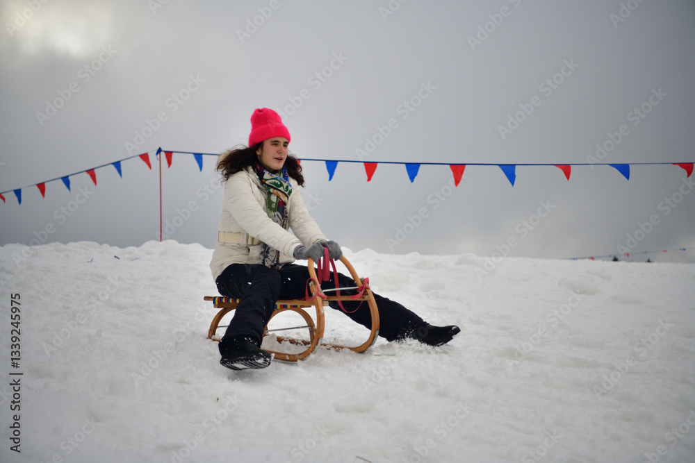 Girl sledding downhill on snow in winter and laughing with joy