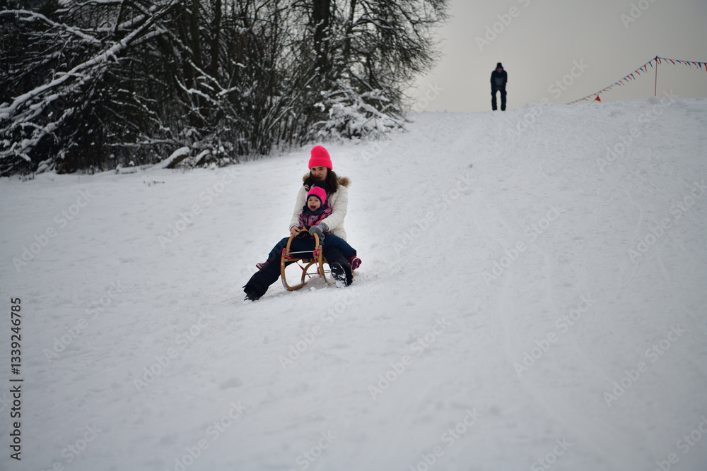 Two girls are tobogganing downhill on snowy hill in winter