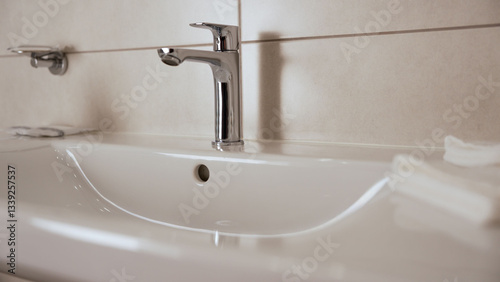 Chrome faucet handle lifting gradually on pristine white ceramic sink, revealing sleek modern bathroom design and minimalist plumbing fixture with smooth metallic surface