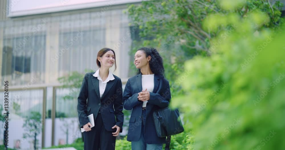 Two cheerful young professional women walking together in an urban park, laughing and chatting. Two cheerful young professional women walking together in an urban park, laughing and chatting.